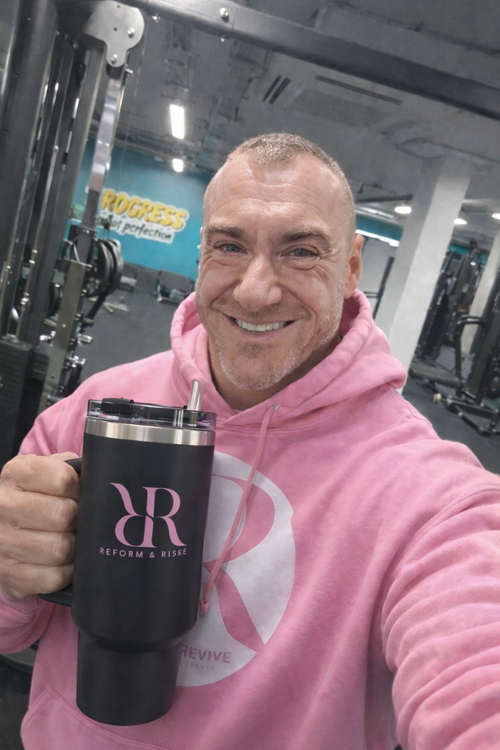 Man smiling in gym holding a 40oz hydration tumbler with handle & lid, wearing a pink hoodie.