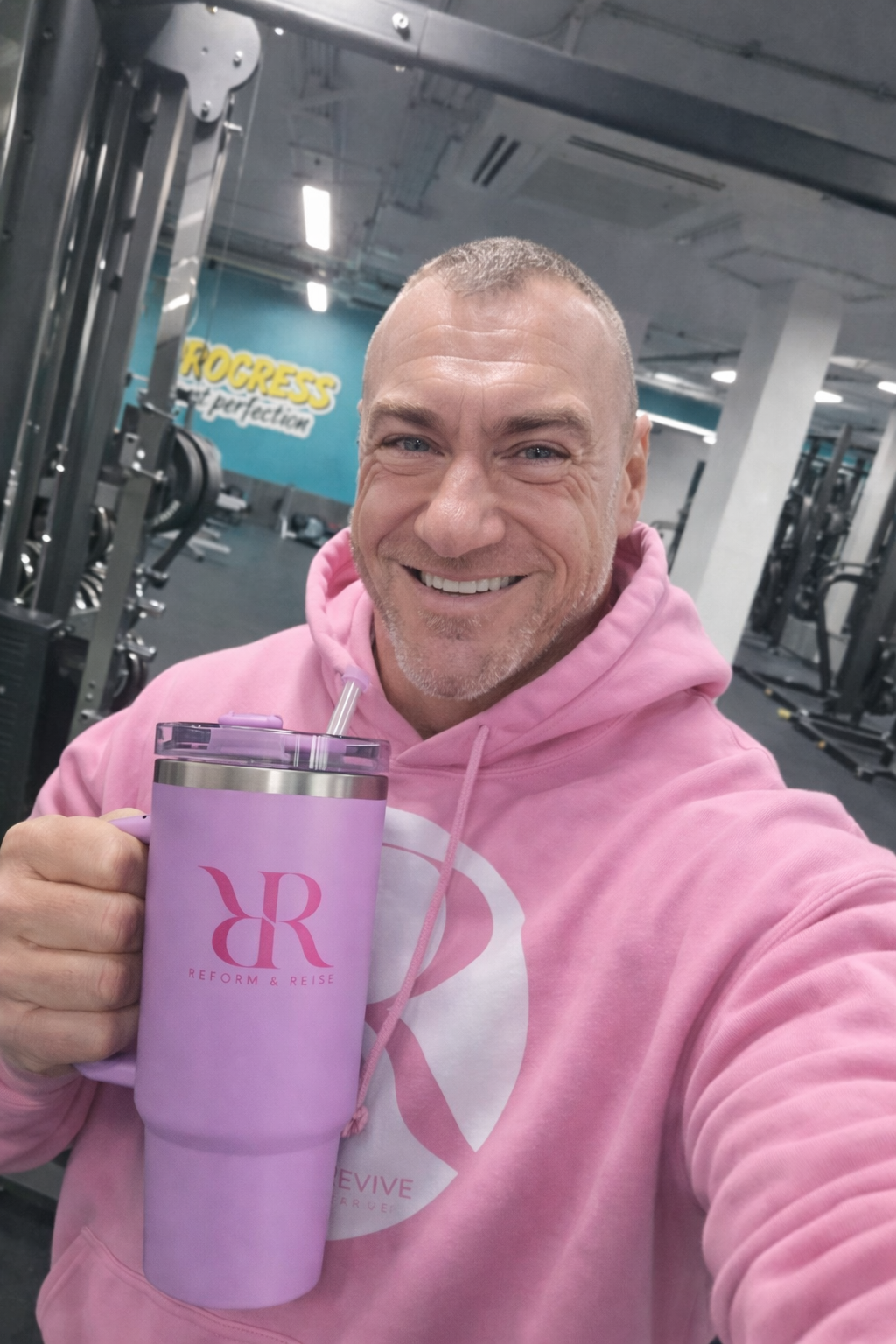 Man smiling in gym holding a 40oz hydration tumbler with handle & lid, wearing a pink hoodie.
