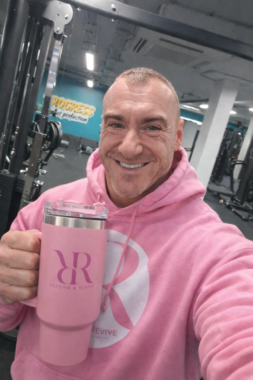 Man smiling in gym holding a 40oz hydration tumbler with handle & lid, wearing a pink hoodie.